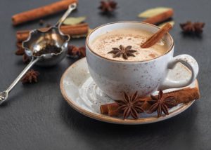 A cup of chai tea made with milk with cinnamon stick and star anise inside cup of chai tea